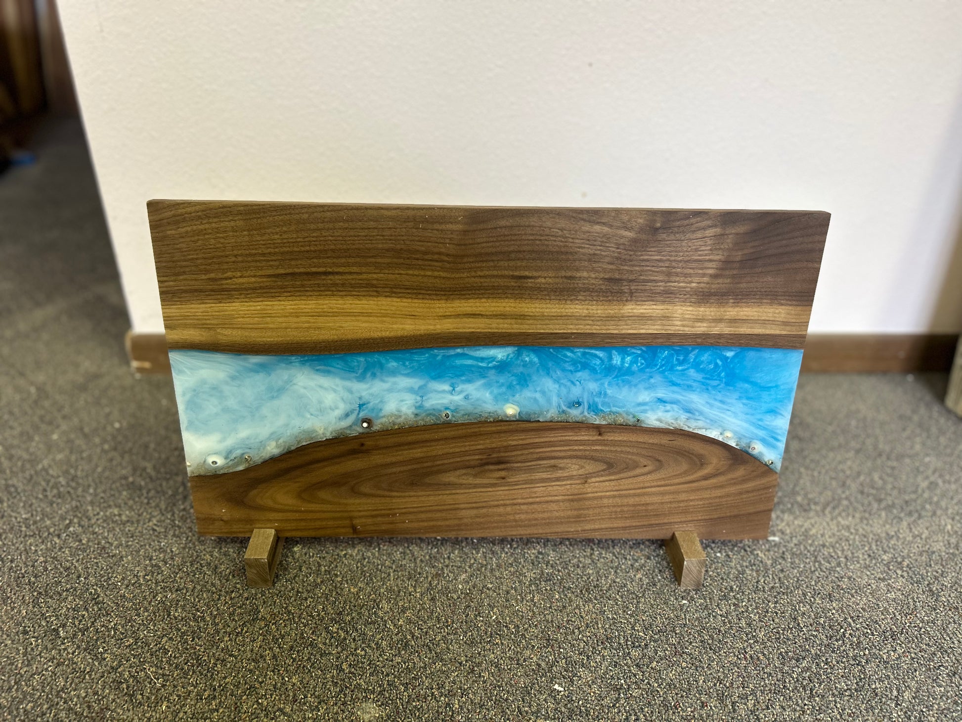 Wooden display stand with a blue resin inlay on a carpeted floor.
